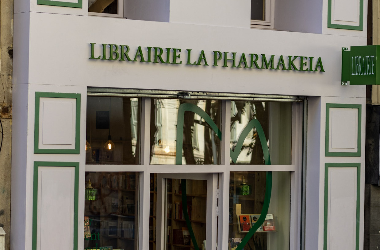 Photo de la devanture mauve avec les motifs et écritures verte de la libraire la pharmakeia,